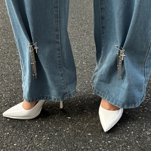 Catena a nappa con croce d'argento e spilla su jeans blu e tacchi bianchi