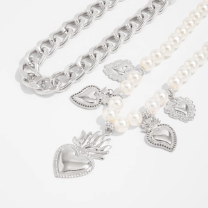 Detailed view of layered silver metal chains and faux pearl necklaces with heart pendants