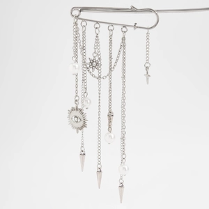 Detail of silver safety pin brooch featuring hanging metal chains and star charms