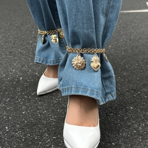 Dettaglio di ciondoli a croce e cuore su una cavigliera dorata sopra jeans blu