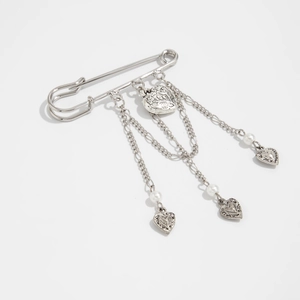 Detailed view of silver safety pin brooch with heart pendants, pearls and metal chains
