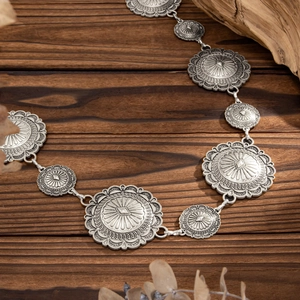 Detailed shot of vintage silver flower discs on a bohemian waist chain over wood