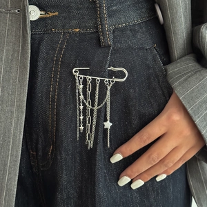 Close-up of silver punk safety pin brooch with star charm and layered chain tassels