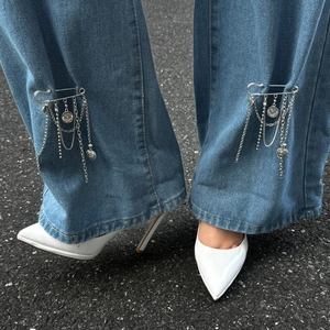 Silver layered tassel pin with heart and coin charms attached to blue denim pants