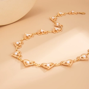 Chaîne de taille dorée avec maillons cœur et perles pour femme sur fond beige