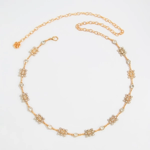 Détail de la chaîne de taille dorée avec strass carrés et pendentif en forme de rose