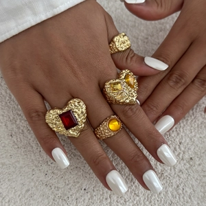 Nahaufnahme von vier goldenen Ringen mit roten und gelben herzförmigen Edelsteinen