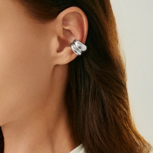 Detailopname van een zilveren ear cuff met onregelmatige textuur en golvend lava-ontwerp