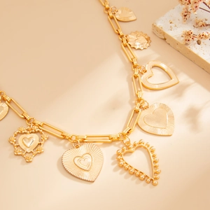 Détail de collier chaîne dorée avec pendentifs cœur évidé sur fond de pierre texturée