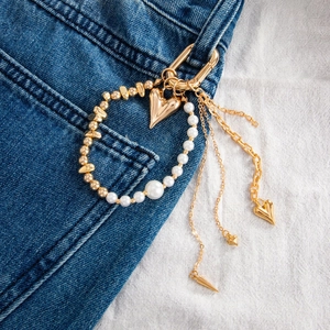 Macro view of gold metal heart charms and pearl bead chains on denim clothing