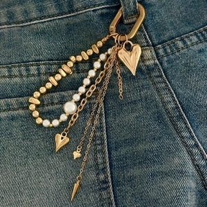 Detail view of multi-layered gold chains with heart charms and pearls on denim jeans