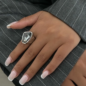 Gros plan d'une bague argentée avec cristal gris sur fond de costume rayé