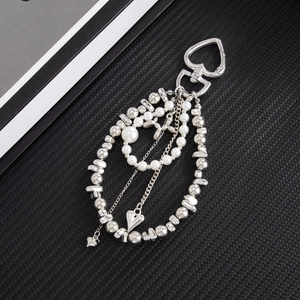 Detail of silver heart clasp with layered faux pearls and metallic charms on black mesh