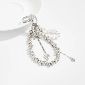 Detail of silver layered bag chain with heart charms and imitation pearls on white ceramic