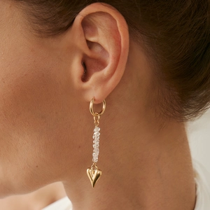 Close-up of golden drop earring with crystal beads and heart pendant on ear