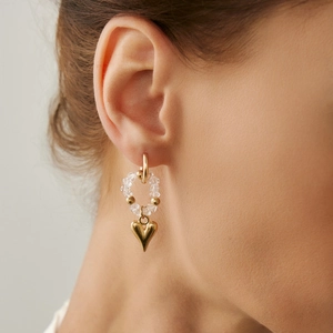 Close-up of golden heart pendant beaded earrings with crystal accents on a model