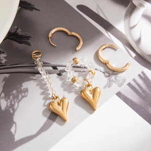 Detailed view of gold heart pendants and beaded hoop earrings on a marble-style book