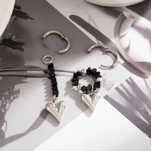Detail showing asymmetrical black beaded heart earrings with silver pendants on magazine