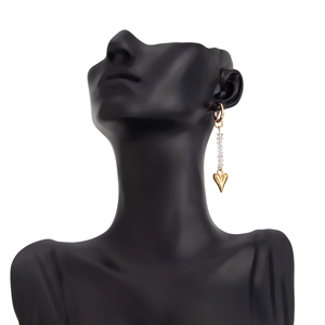 Close-up of long gold earrings with crystal beads and heart pendants on black bust