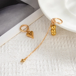 Detailed shot of asymmetric gold earrings with heart pendant and long beaded chain tassel