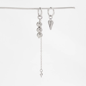 Detail of silver asymmetric earrings featuring heart pendant and long beaded tassel chain