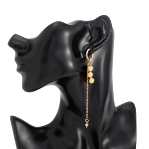 Detail of gold tassel earring with metal beads and conical pendant on black mannequin