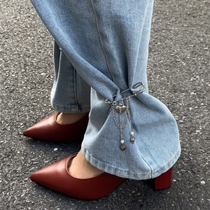 Detail of silver heart charm and metal chain pin cinching light blue denim jeans