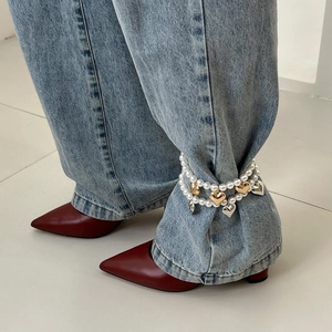 Détail d'une chevillère en perles avec breloques cœur portée sur un jean bleu