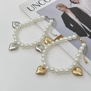 Détail d'un ensemble collier et bracelet en perles avec pendentifs coeurs sur fond de mode