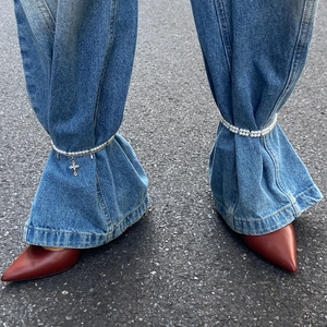 Détail de la sangle en perles avec croix utilisée comme attache décorative pour jeans