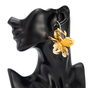 Makroansicht goldener Blumenohrringe mit gehämmerter Metallstruktur am Modell getragen