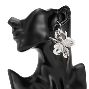 Details großer silberner Blumenohrringe mit gehämmerter Metallstruktur auf Harzblättern