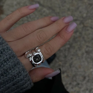 Gros plan d'une bague argentée massive ornée d'une pierre noire carrée sur un doigt