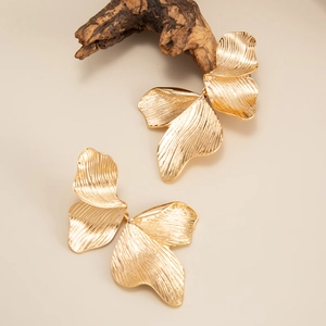 Detailopname van gouden blad oorbellen met textuur op een rustieke houten achtergrond