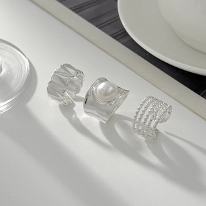 Close-up of three liquid metal rings featuring a wide crinkled texture and faux pearl inlay