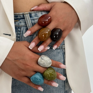 Close-up of trendy wide resin rings in diverse amber and marble colors worn by a model