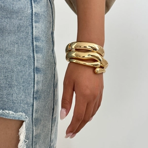 Polished gold drop bangle on wrist featuring a bold fluid geometric spiral design