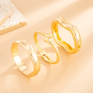 Close-up of three gold water-drop and wavy geometric bangles with polished finish