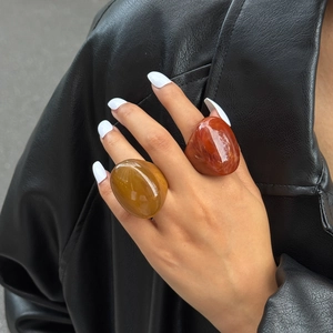 Detail view of bold amber and reddish brown resin rings worn with a stylish leather jacket