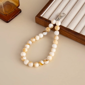 Detail of beaded bag chain with creamy white and amber acrylic beads on a wooden tray