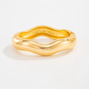 Macro shot of polished gold-plated wave hinge bangle with smooth mirror finish surface