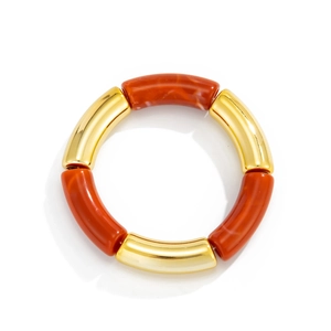 Detalle de pulsera de tubos metálicos dorados y resina naranja con texturas de mármol