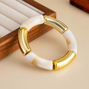 Detalle de pulsera elástica estilo bambú de metal dorado y resina jaspeada crema