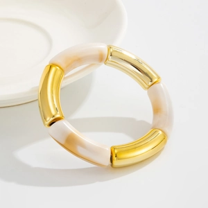 Detalle de la pulsera elástica con tubos de metal dorado y segmentos de resina jaspeada