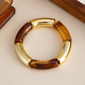 Detalle de una pulsera elástica con resina ámbar y tubos de metal dorado pulido