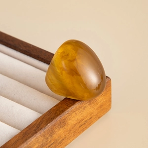 Macro detail of wide amber resin ring with fluid marble patterns on a wooden display