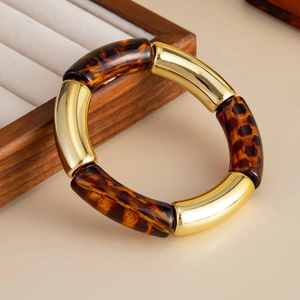 Detalle de pulsera elástica estilo bambú con segmentos de metal dorado y resina de leopardo