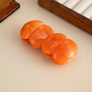 Detail of orange marble texture on resin hair claw clip with glossy finish and wood stand