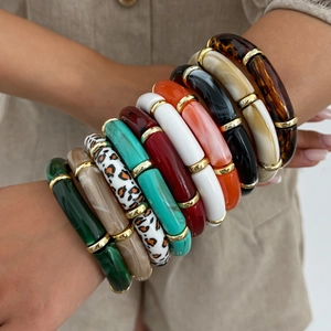 Close-up of stacked acrylic bamboo bracelets with colorful marble textures and gold spacers