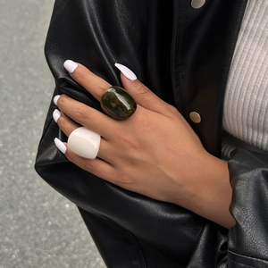 Detail of wide resin rings in marble brown and glossy white on model wearing leather jacket